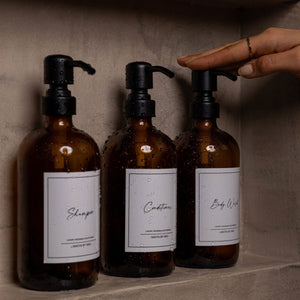 NIKITA amber glass dispenser bottle set with stainless steel pumps for your bathroom. Durable soap dispensers with waterproof labels for shampoo, conditioner and body wash. Ideal new home gift for her or gift for couple.
