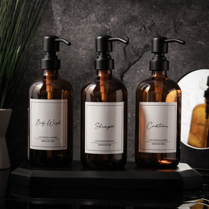 NIKITA amber glass dispenser bottle set with stainless steel pumps for your bathroom. Durable soap dispensers with waterproof labels for shampoo, conditioner and body wash. Ideal new home gift for her or gift for couple.