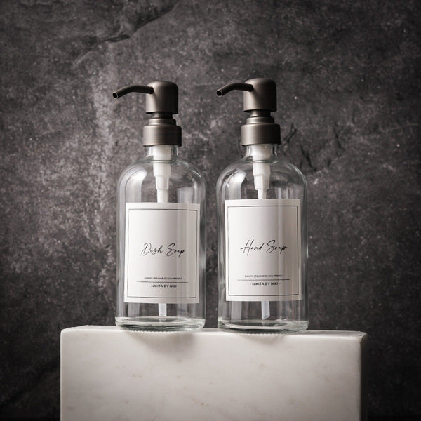 NIKITA clear glass dispenser bottle set with stainless steel pumps for your kitchen or bathroom. Durable soap dispensers with waterproof labels for hand soap, dish soap, hand lotion or hand sanitiser.