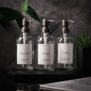 NIKITA clear glass dispenser bottle set with stainless steel pumps for your bathroom. Durable soap dispensers with waterproof labels for shampoo, conditioner and body wash. Ideal new home gift for her or gift for couple.